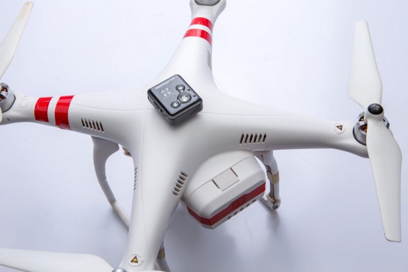 White and red drone lying on a white surface with a small camera device attached, clean studio setting